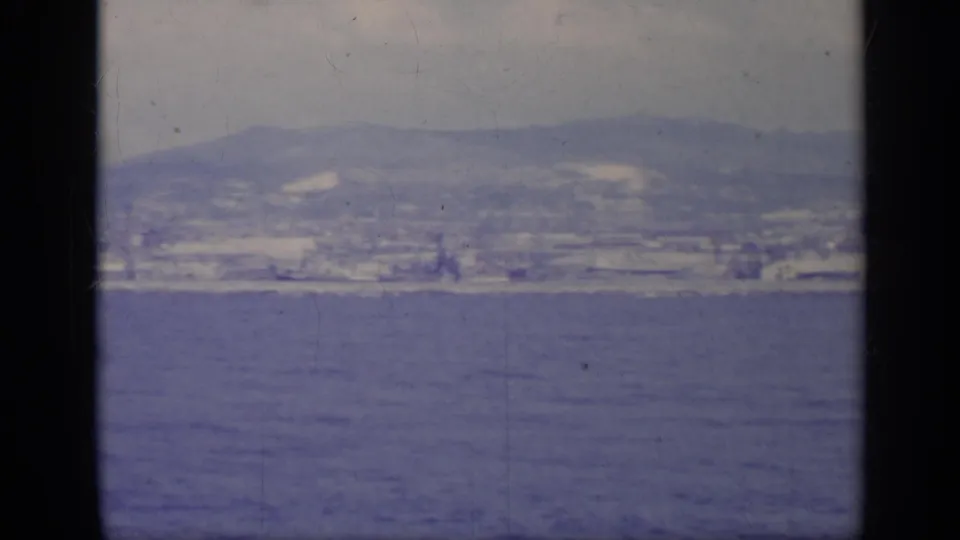 1962 Italy coastal view across blue water, showing a soft distant city line and mountains within dark 8mm frame borders.