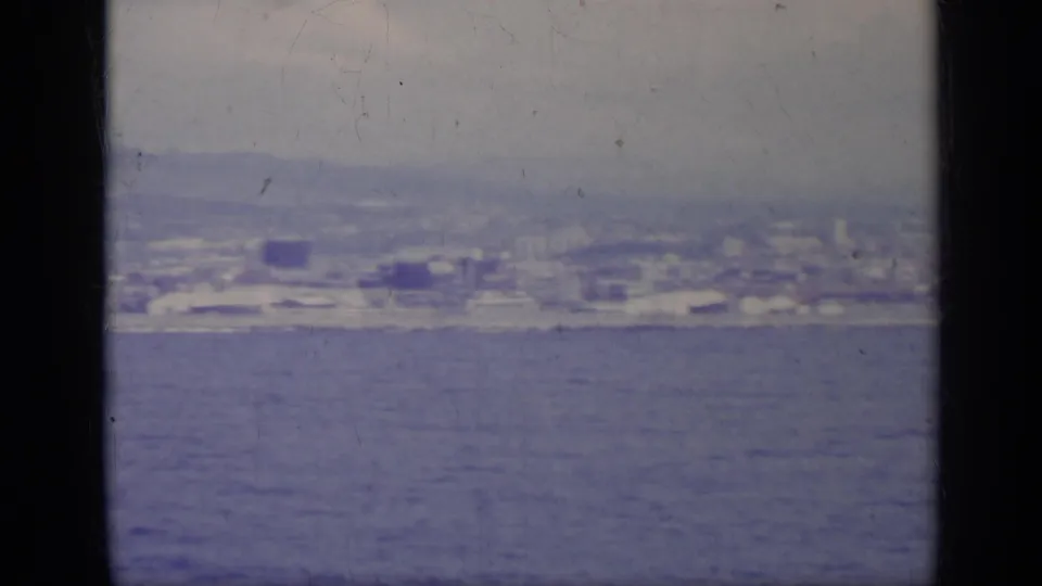 Distant Italian coastal buildings and hills appear across the water in a soft, purple-blue 8mm frame.