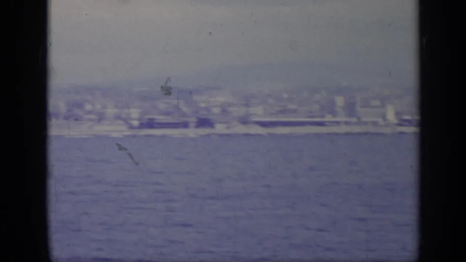 Distant Italian waterfront and low hills viewed across the sea in a worn 8mm travel-film frame.