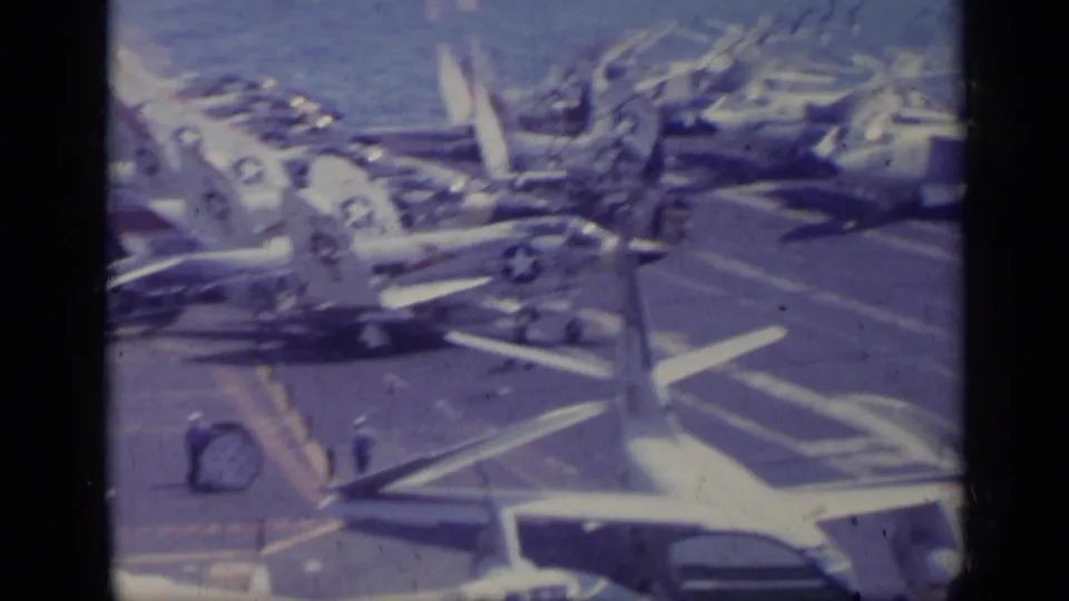 1962 8mm view of multiple U.S. Navy aircraft on a carrier deck, with small uniformed figures visible among the planes.