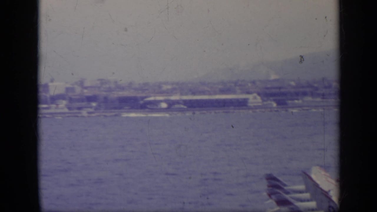 Distant Italian bay with parked aircraft near a waterfront and hazy hills behind.