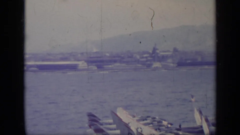 1962 Italian waterfront view with aircraft partly visible at lower right and industrial buildings across the water.