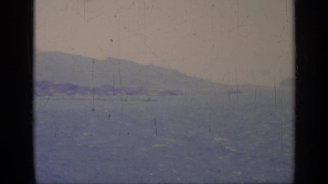 Hazy sea view with a distant island or headland framed by dark film edges.