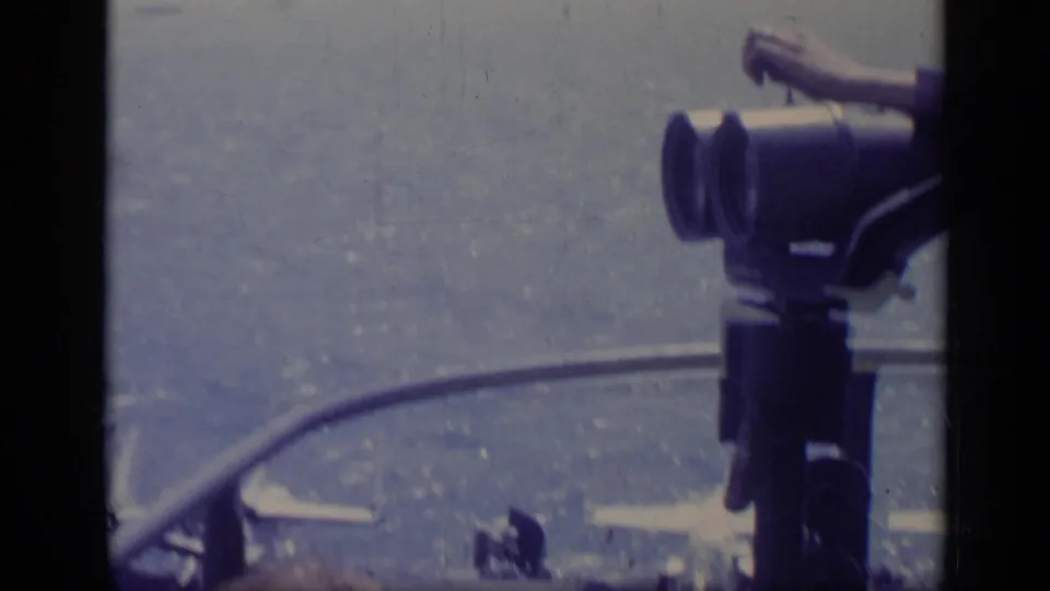 A tourist's arm and mounted binoculars are seen above a hazy Italian seaside view in 1962 8mm footage.