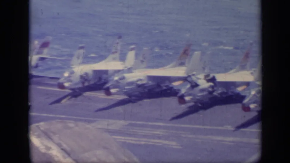 Multiple white jet fighters appear lined up on a carrier deck in 1962 Italy footage, with ocean visible beyond the aircraft.