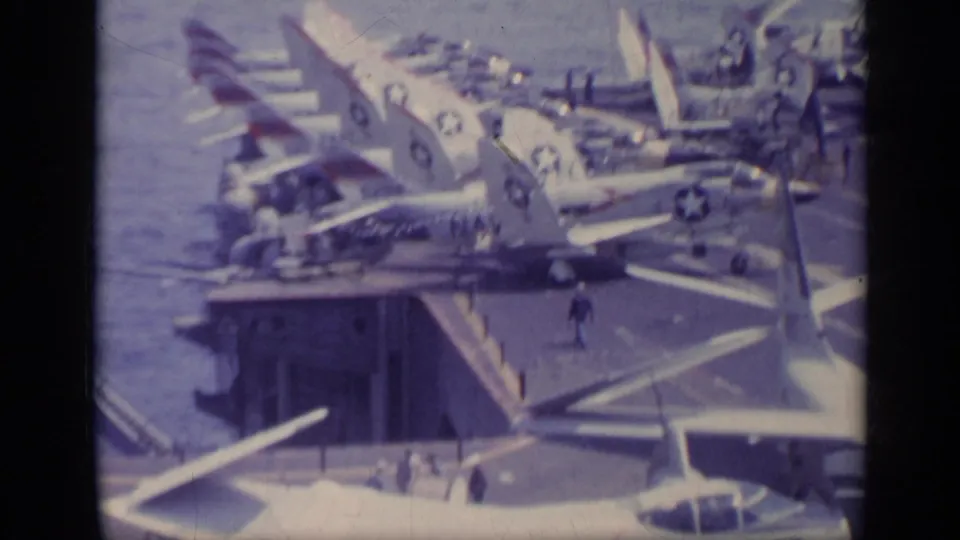 1962 8mm carrier-deck shot near Italy showing military aircraft beside a deck opening, with crew figures and sea in the background.