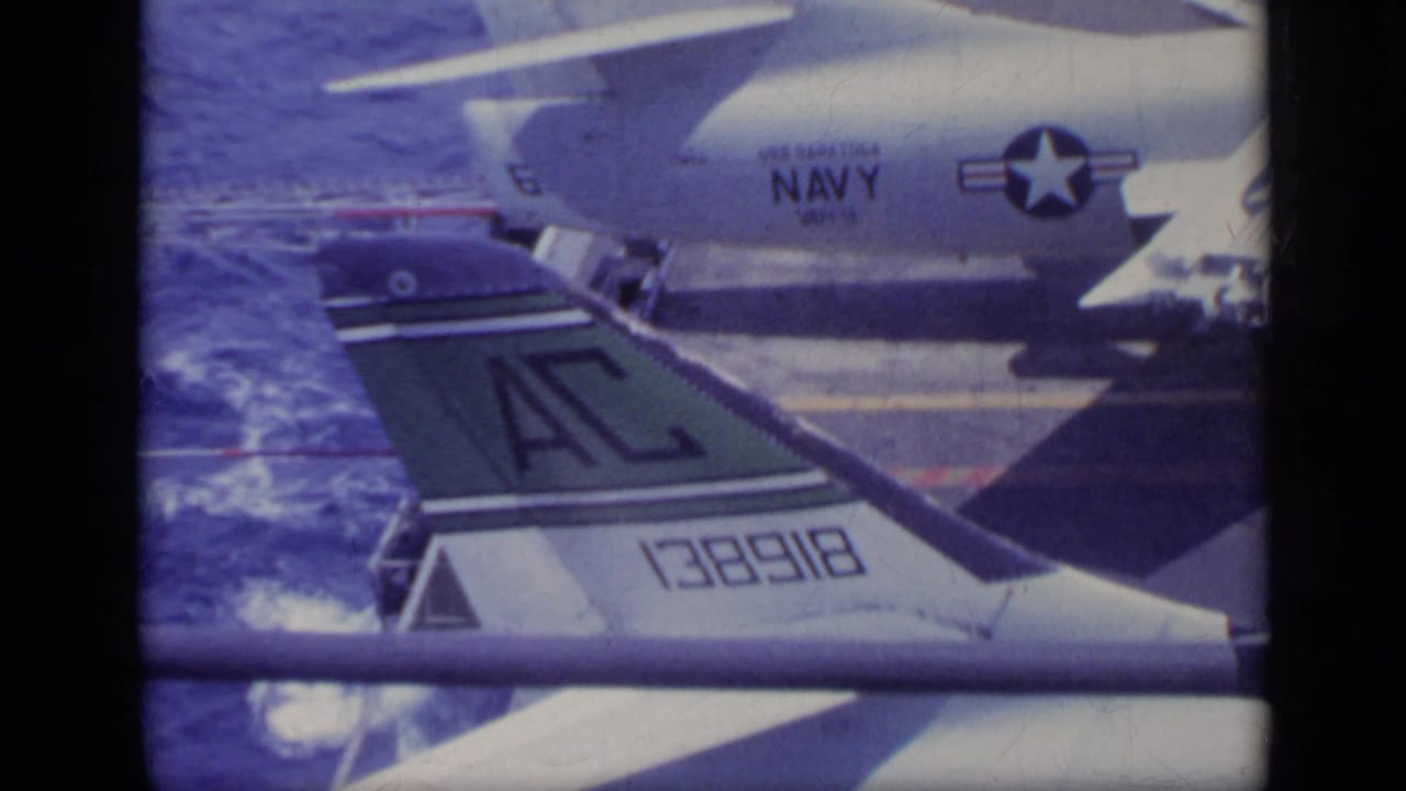 1962 Italy home-movie frame showing a Navy-marked aircraft tail and fuselage detail beside open sea.