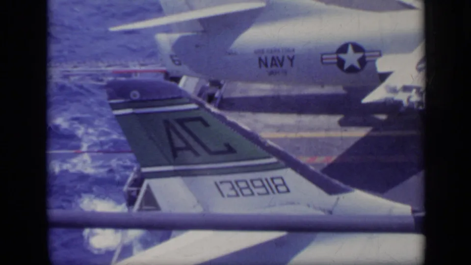 1962 Italy home-movie frame showing a Navy-marked aircraft tail and fuselage detail beside open sea.