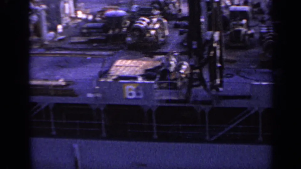 1962 Italy 8mm frame looking across a working ship deck with equipment, crew figures, railings, and a visible numbered panel.