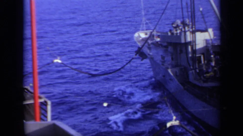1962 home-movie footage shows the bow and deck of a white ship near Italy, with cables or hoses extending over the water.