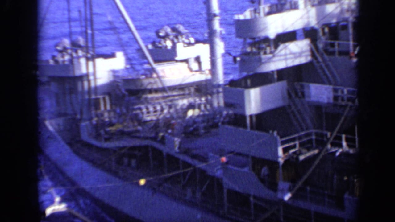 1962 8mm view near Italy showing the upper deck of a cargo ship with railings, mast structures, and open water in the background.
