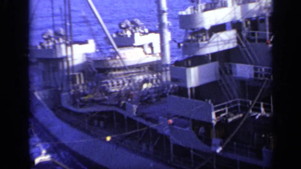 1962 8mm view near Italy showing the upper deck of a cargo ship with railings, mast structures, and open water in the background.