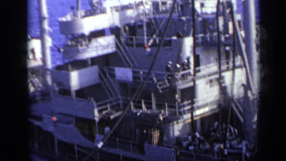 High-angle 1962 8mm frame of a cargo vessel near Italy, showing superstructure, railings, rigging, and deck equipment at sea.