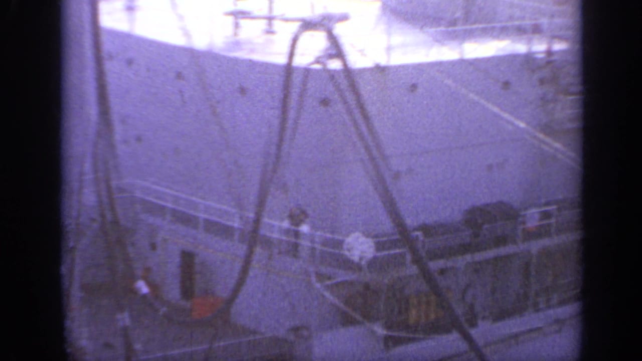 Large ship deck with railings, cables, and rigging seen through soft purple-tinted film.