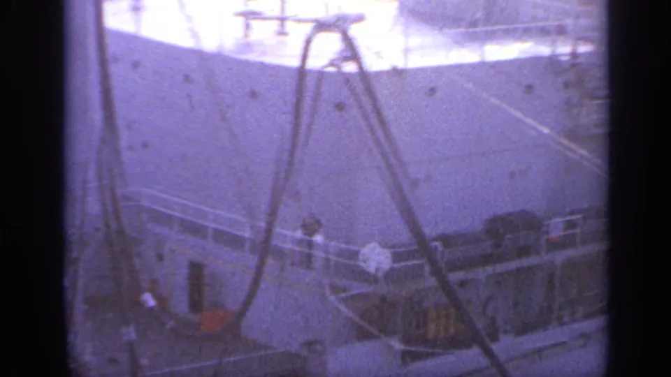 1962 Italy 8mm view of a large vessel deck with railings, hanging cables, and rigging under hazy light.
