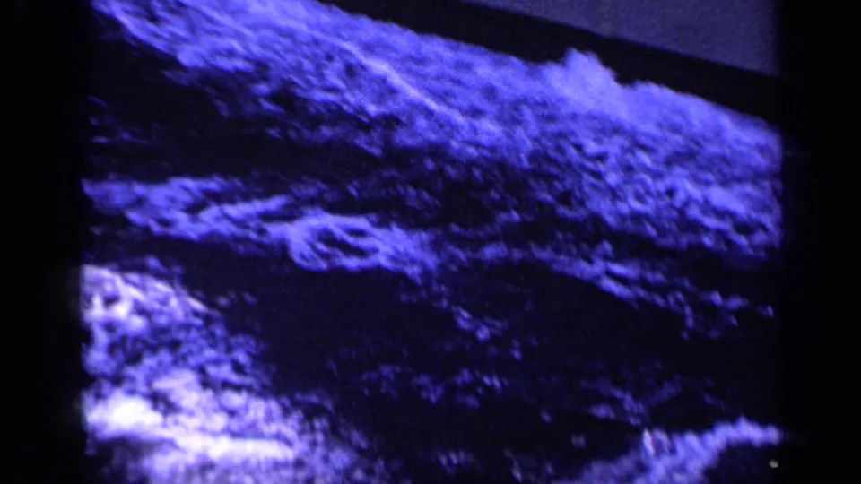 1962 Italy 8mm view of rough, foaming water passing alongside a dark ship structure.