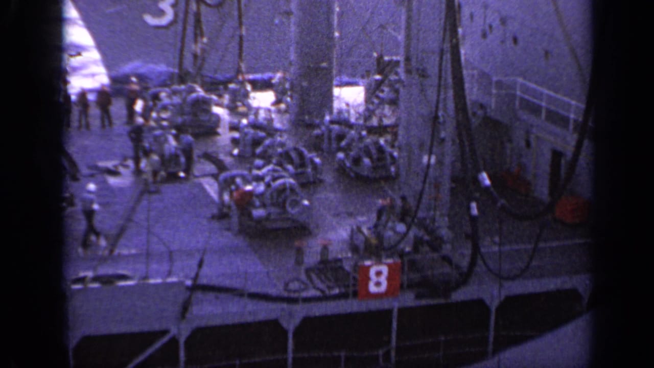 Gray ships and deck activity seen through dark film borders and rigging.