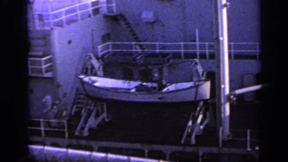1962 Italy 8mm frame showing a mounted lifeboat, deck stairs, white railings, and part of a passenger ship side.