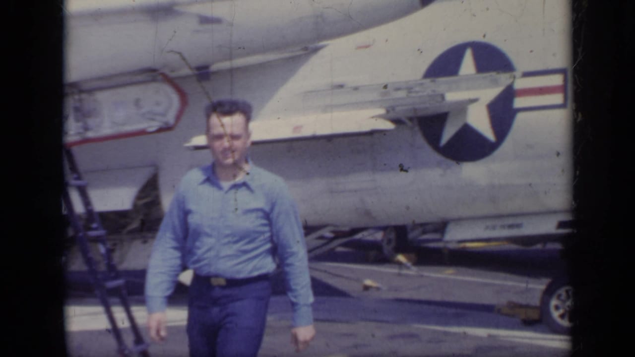 Man walks toward the camera in front of a military jet fuselage.