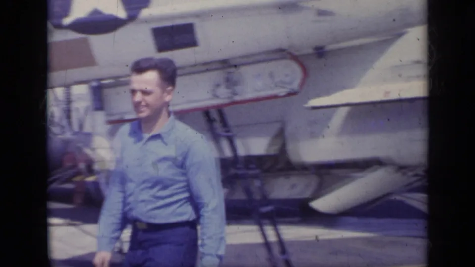 The home-movie frame shows the man moving past the jet, with landing gear and wing details visible behind him.