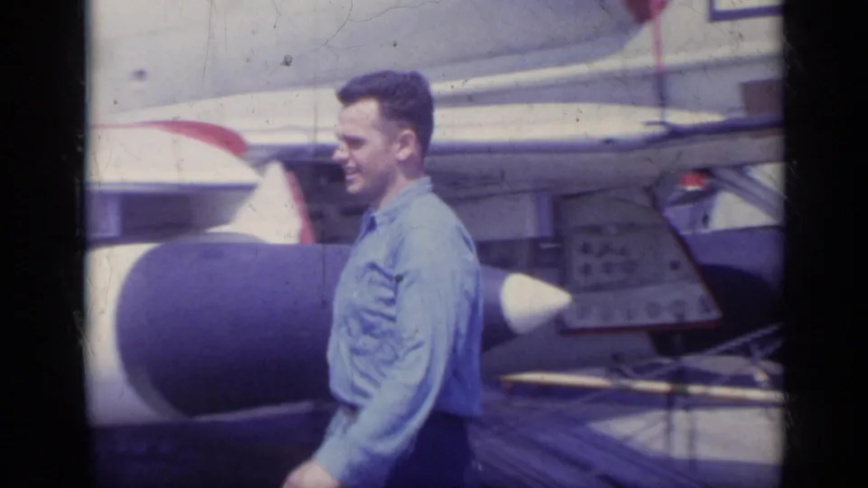 A side view captures the smiling man walking beside the jet, with the aircraft nose, wing area, and airfield equipment behind him.