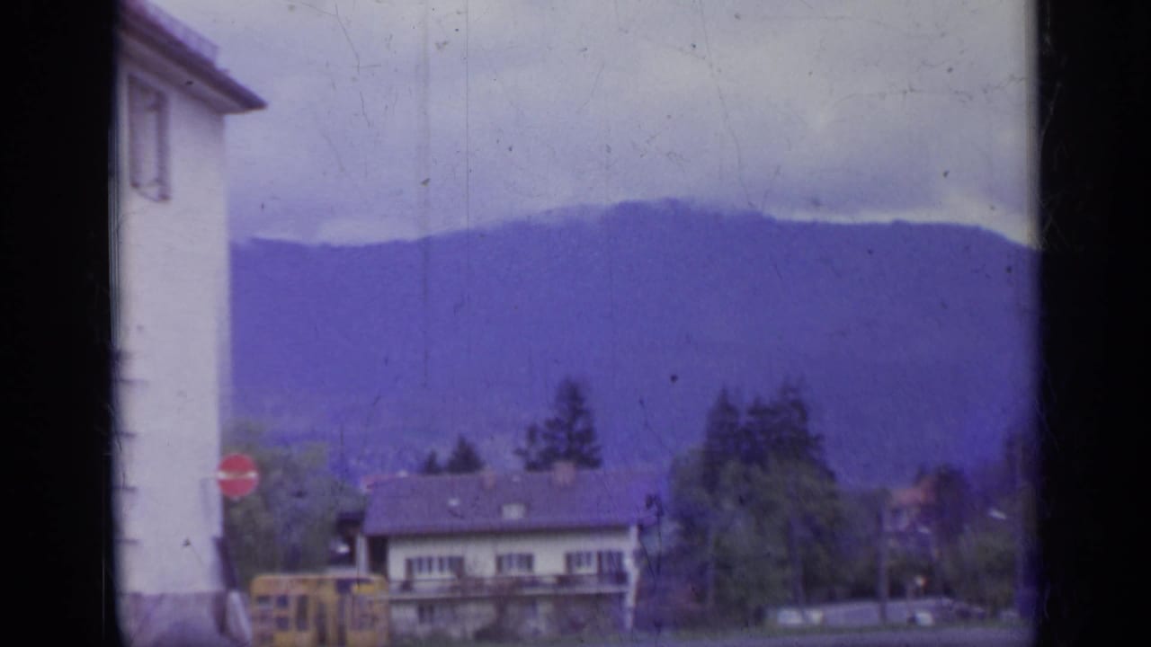 Street view with white building edge, yellow bus, red stop sign, houses, trees, and hazy mountain ridge.