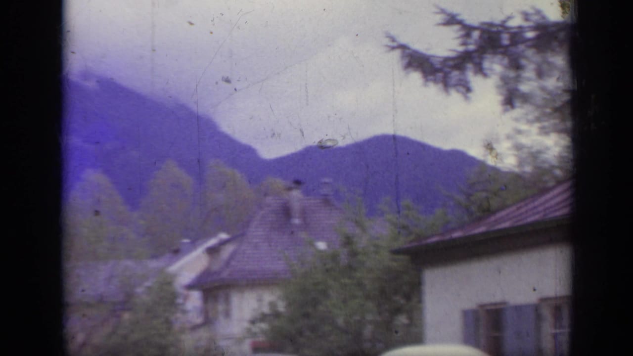 Houses with tiled roofs below purple-toned hills and trees.