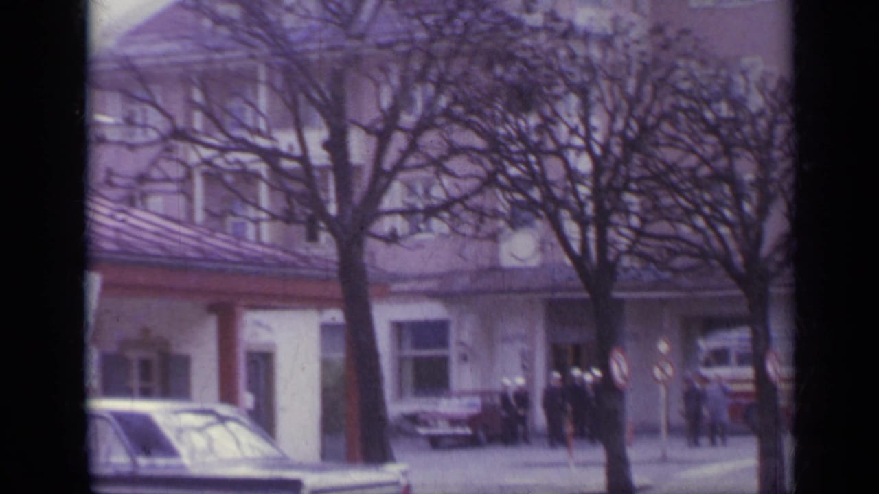 Street-side resort building with bare trees, cars, and small distant pedestrians.