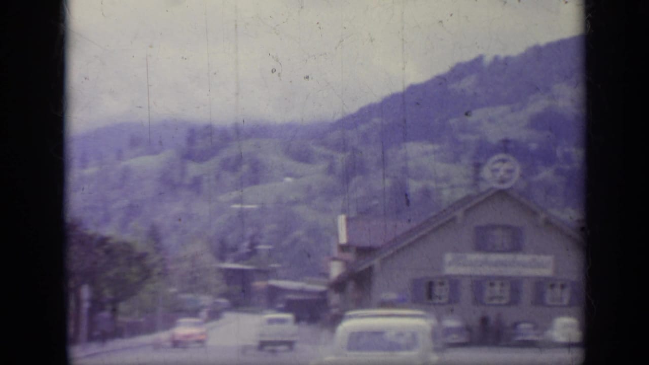 Alpine town street seen through dark window bars with hills behind it.