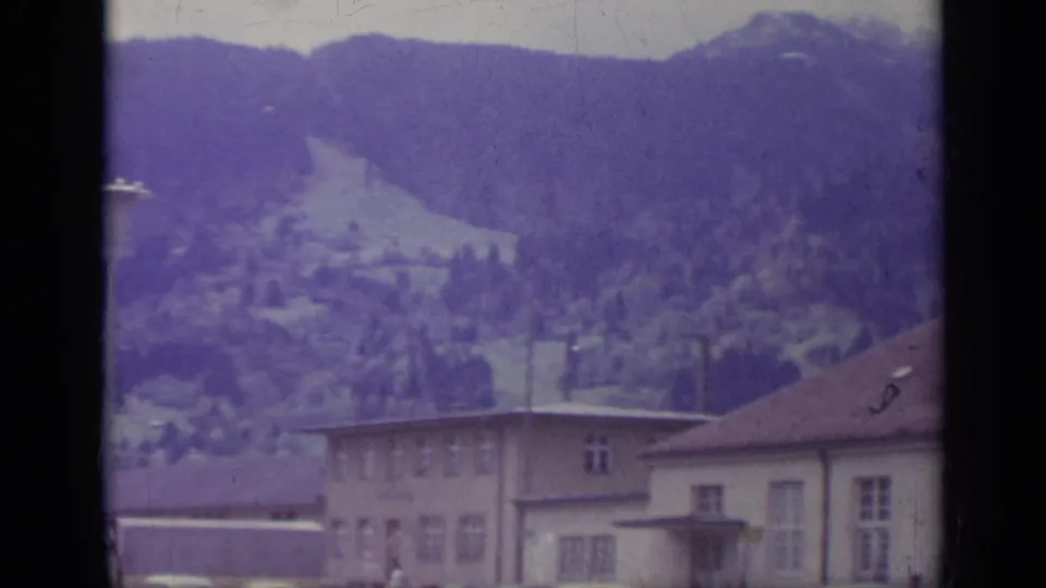Italian alpine town buildings and rooftops below a dark wooded mountainside, filmed in soft, color-shifted 8mm.