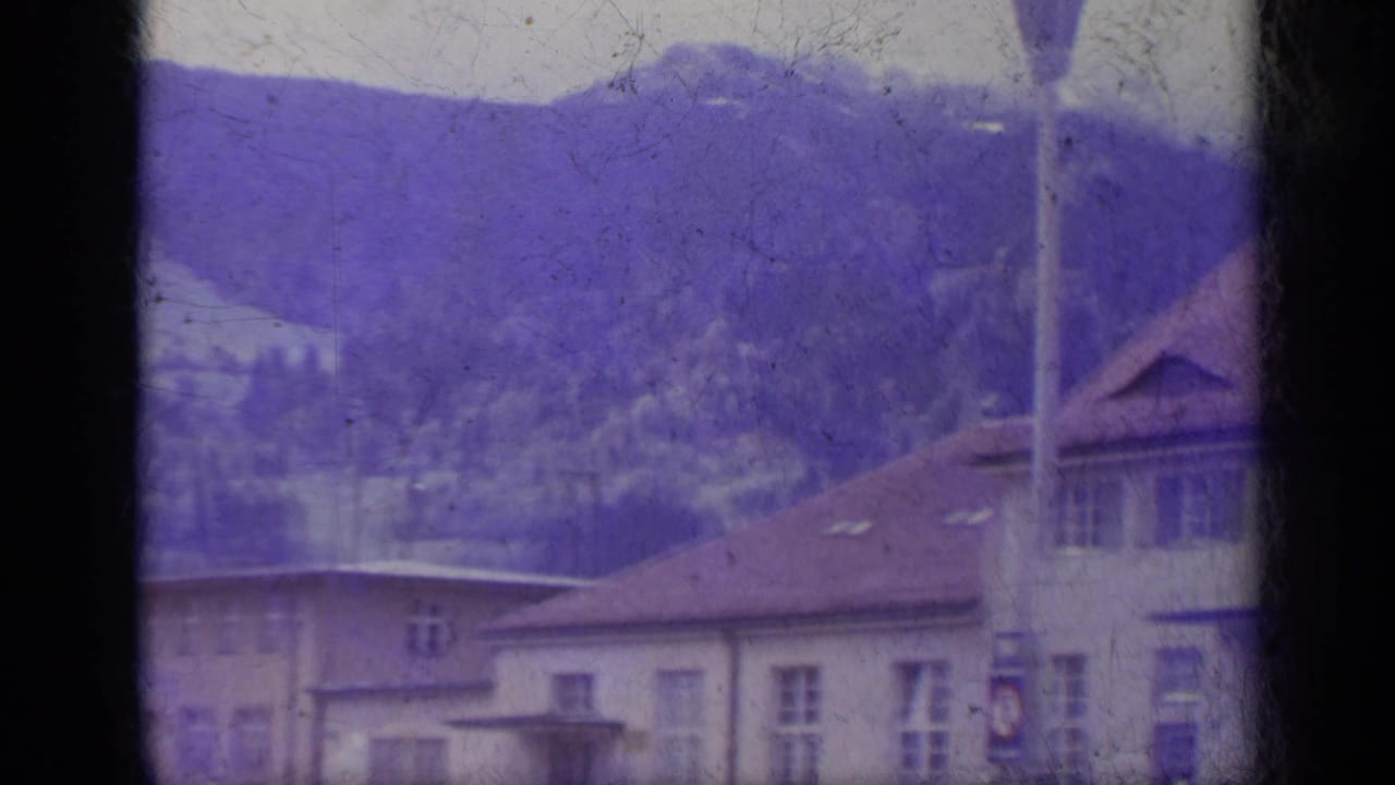 Mountain town buildings with terracotta roofs seen through dark film gate edges.