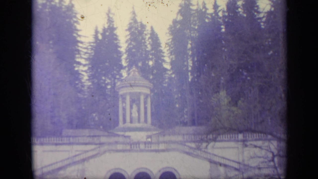 Columned pavilion and grand stair monument surrounded by tall evergreen trees.