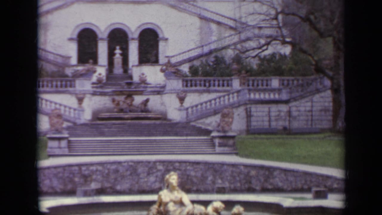 Stone staircase and arched facade above a reflective fountain pool.