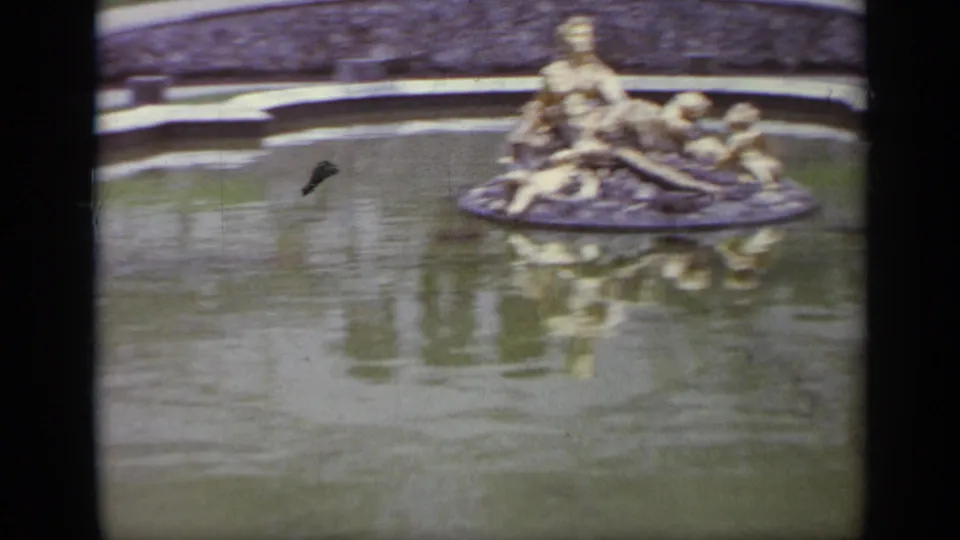 1962 Italy 8mm frame centered on a gilded classical fountain group reflected in the surrounding pool.