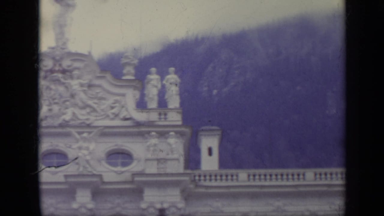 Upper palace facade with statues, balustrade, and purple-toned mountain slope behind.