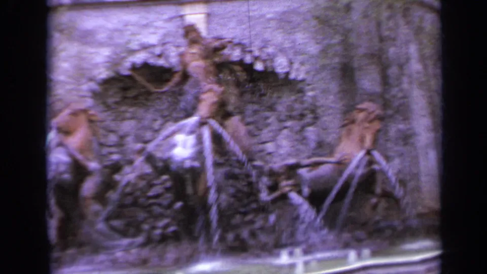 1962 Italy 8mm frame showing ornate fountain sculptures, horse forms, water streams, and a curved basin in a purple-tinted scan.