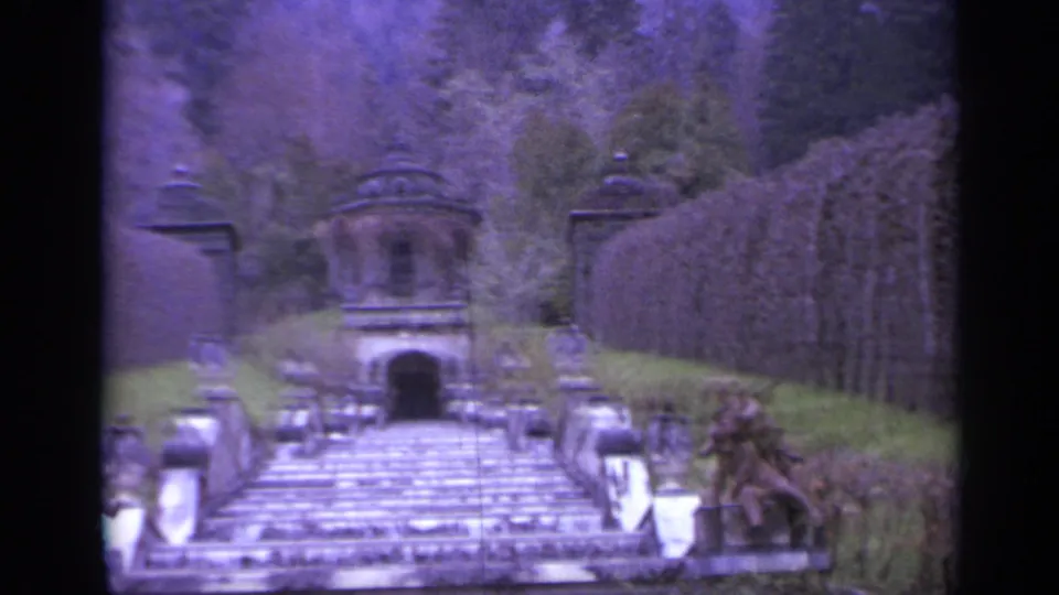 1962 Italy 8mm frame showing a stone stairway, balustrades, small pavilion, statues, and trellis-lined garden slopes.