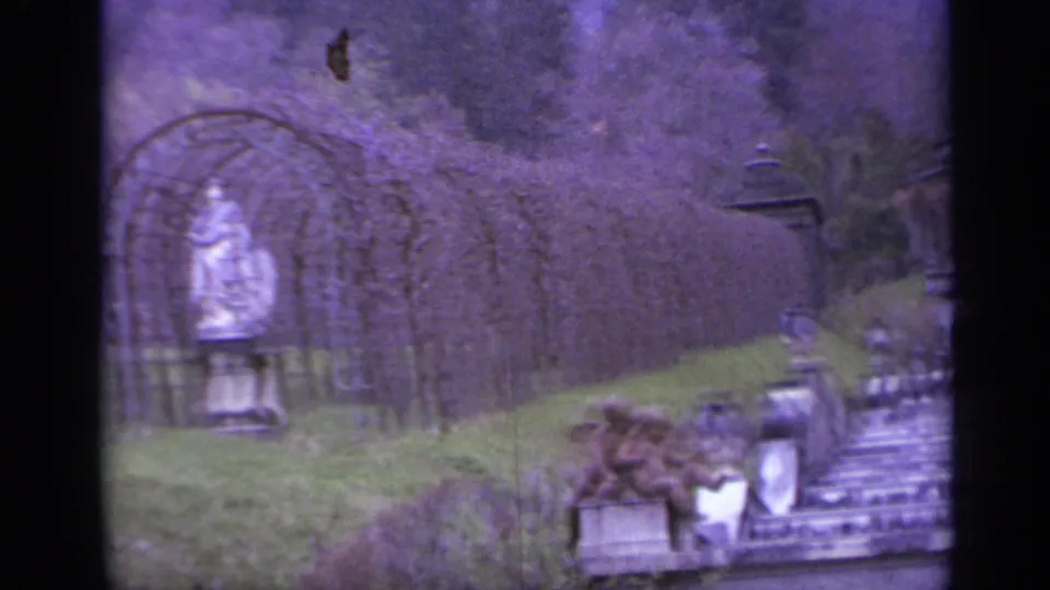 1962 Italy 8mm frame with a trellis arch, statue-like figure, stone garden features, fountain edge, and sloped greenery.