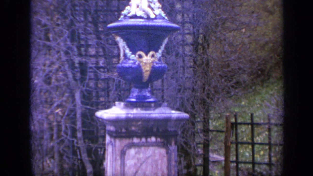 1962 Italy 8mm frame showing a formal garden detail with an ornate urn, bare hedges, latticework, and soft home-movie color.
