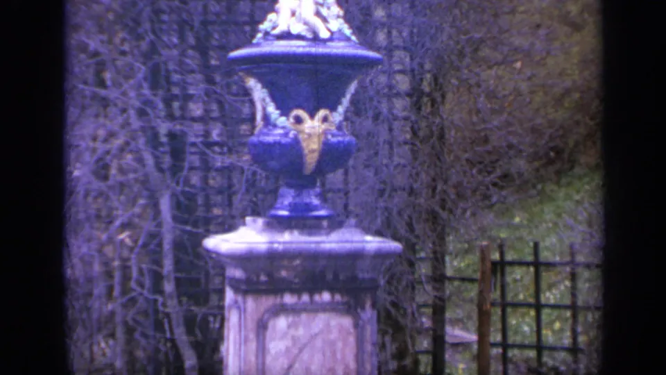 1962 Italy 8mm frame showing a formal garden detail with an ornate urn, bare hedges, latticework, and soft home-movie color.