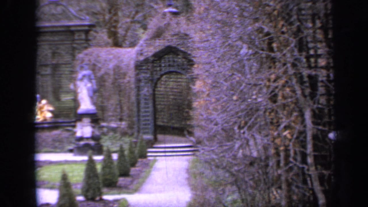 Garden path leading toward an arbor with statues and clipped hedges nearby.