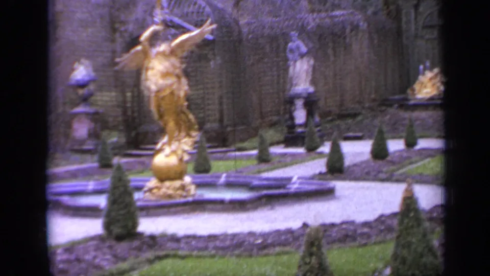 1962 Italy home-movie frame centered on a gold-colored fountain sculpture, with formal paths, topiary, and stone statues behind it.