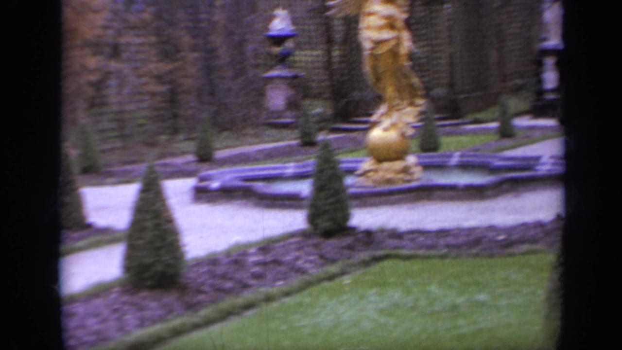 Formal garden path with clipped shrubs, lawn, and a gilded statue near a fountain.