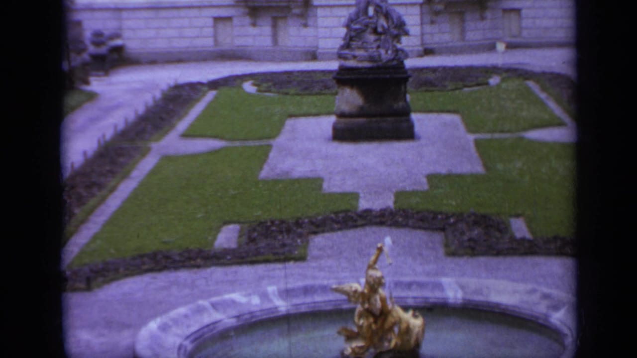 Formal courtyard with lawn paths, a central monument, and a golden fountain figure in the foreground.