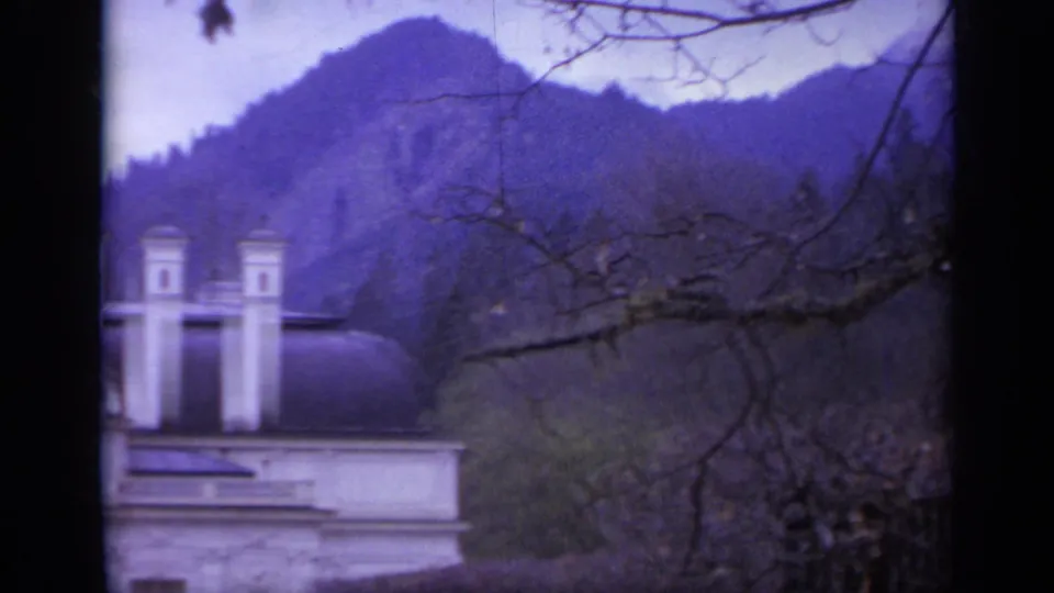 1962 Italy 8mm frame looking past an ornate roof and bare branches toward wooded mountain slopes in the surrounding area.