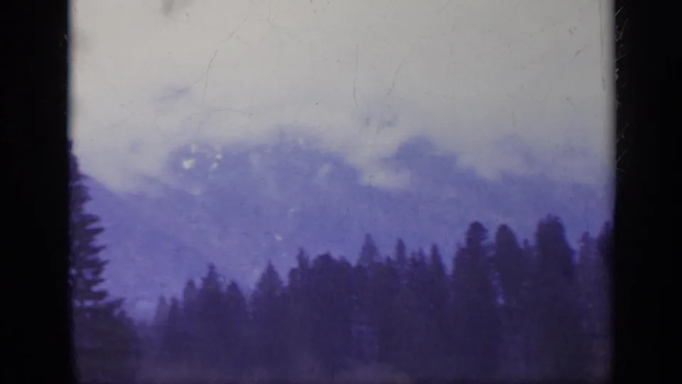 1962 Italy home-movie frame with a clouded mountain backdrop and a dense forest silhouette in the foreground.