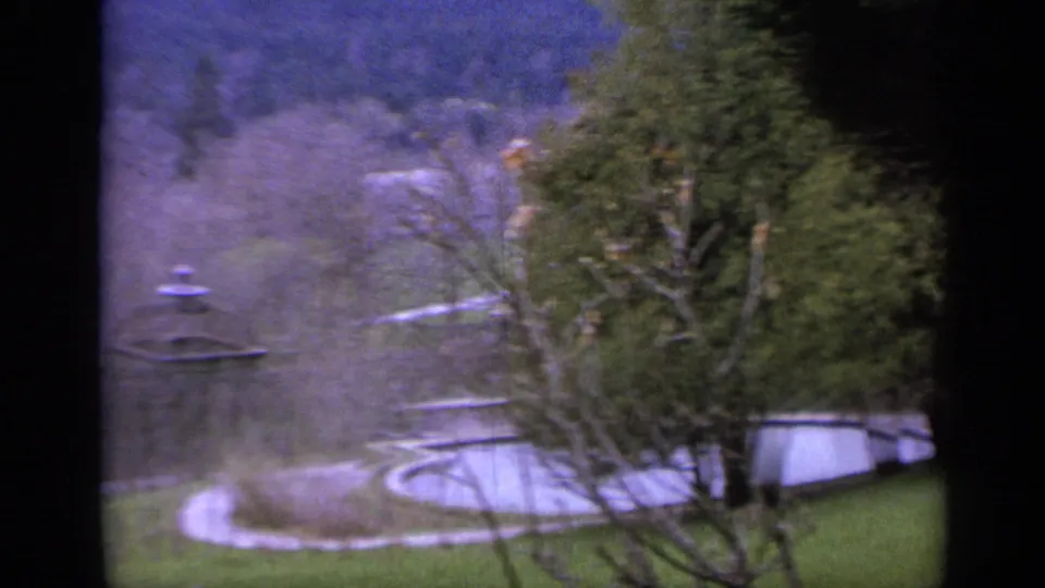 Italian countryside garden view with curved paths, lawn, bare trees, evergreens, and a small gazebo-like structure.