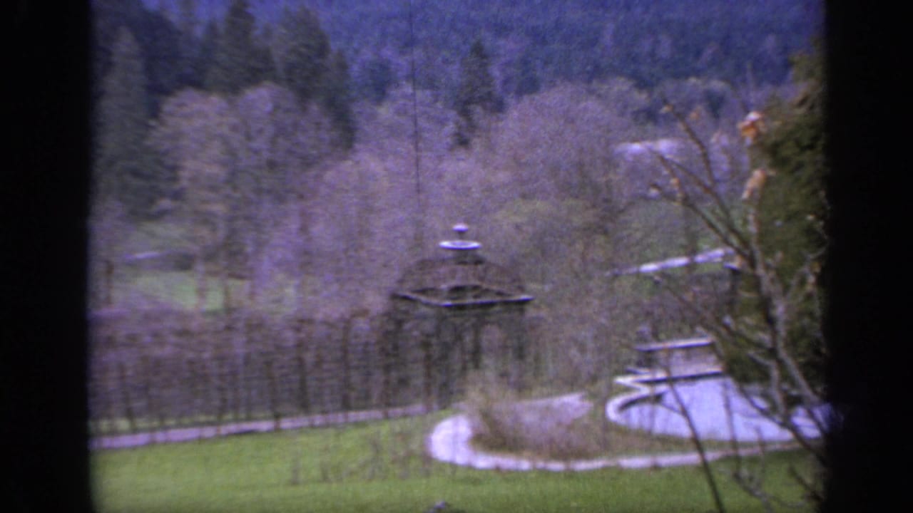 Distant estate grounds with a fountain, curving path, trees, and wooded hillside.