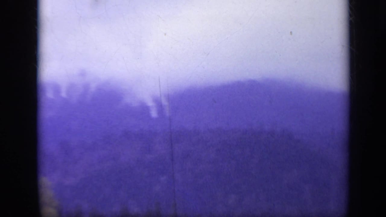 1962 Italy 8mm frame showing a hazy forested mountain ridge with dark gate edges, purple color cast, and visible scratches.