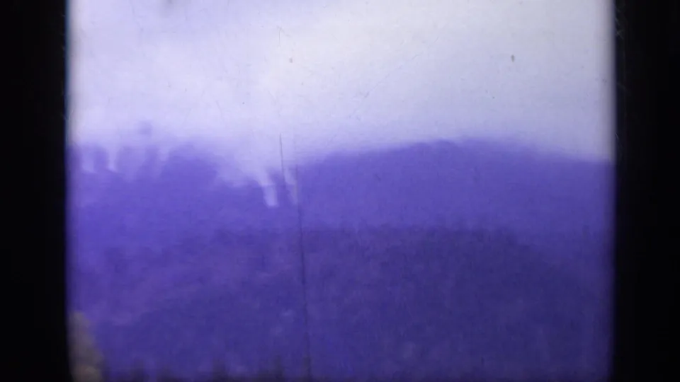 1962 Italy 8mm frame showing a hazy forested mountain ridge with dark gate edges, purple color cast, and visible scratches.